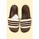 Step into a warm, vintage-inspired style with these Brown & Cream 3-Stripe Slides. Featuring a rich brown footbed and strap detailed with cream triple stripes, they bring a fresh twist to the iconic Adilette design. The soft, cushioned sole and slip-resistant textured outsole make them perfect for everyday wear — whether you’re lounging indoors or enjoying sunny outdoor strolls. Lightweight, water-friendly, and built for comfort with flair. Features: Stylish brown base with cream 3-stripe detailing Cushioned footbed for long-lasting comfort Light blue textured outsole for traction and durability Lightweight and easy to wear Water-resistant synthetic construction ADIDAS ADILETTE BROWN CREAM 3 STIPE SLIDE