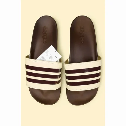 Step into a warm, vintage-inspired style with these Brown & Cream 3-Stripe Slides. Featuring a rich brown footbed and strap detailed with cream triple stripes, they bring a fresh twist to the iconic Adilette design. The soft, cushioned sole and slip-resistant textured outsole make them perfect for everyday wear — whether you’re lounging indoors or enjoying sunny outdoor strolls. Lightweight, water-friendly, and built for comfort with flair. Features: Stylish brown base with cream 3-stripe detailing Cushioned footbed for long-lasting comfort Light blue textured outsole for traction and durability Lightweight and easy to wear Water-resistant synthetic construction ADIDAS ADILETTE BROWN CREAM 3 STIPE SLIDE
